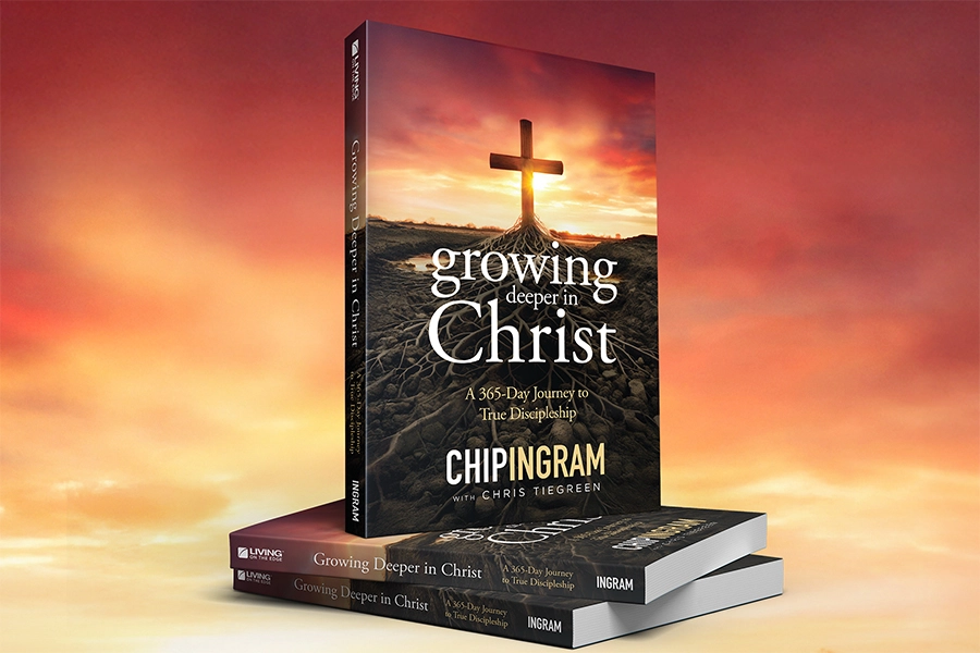 A stack of the devotional book "Growing Deeper in Christ" by Chip Ingram and Chris Tiegreen, featuring a cover with a cross rooted in the earth against a sunset sky.