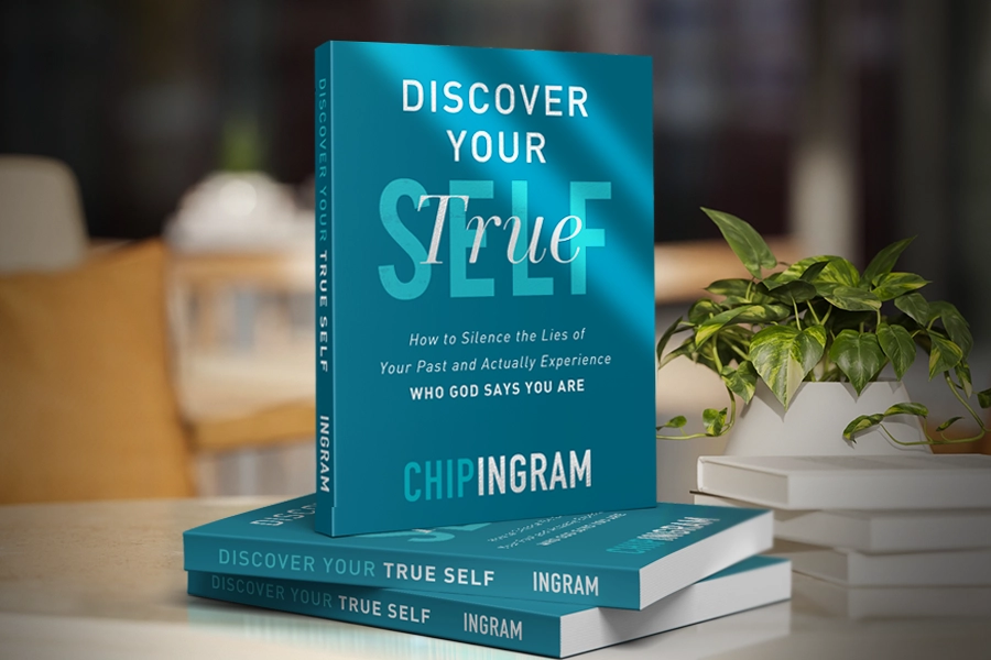 A stack of the book "Discover Your True Self" by Chip Ingram on a white table next to a potted plant.