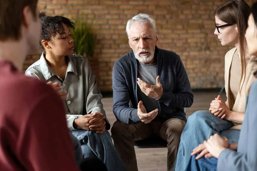 An elderly man sharing his thoughts and feelings with a group of people
