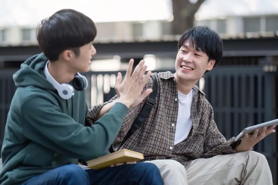 Two male college students chatting outdoors and high-fiving each other.
