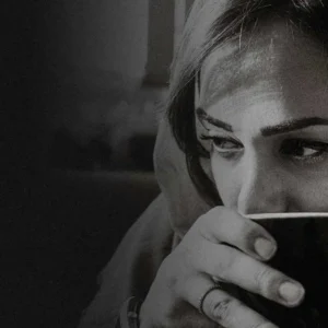 Close-up black and white portrait of a woman thoughtfully holding a coffee mug.