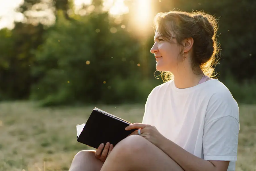 Woman smiling and holding a Bible outdoors in warm sunlight.