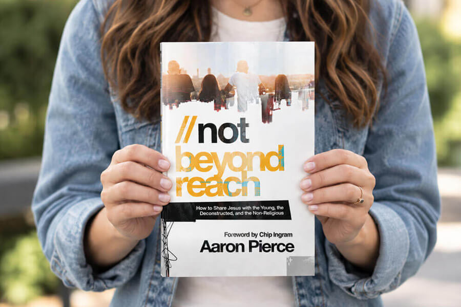 A person wearing a denim jacket holds up a copy of the book "Not Beyond Reach" by Aaron Pierce.