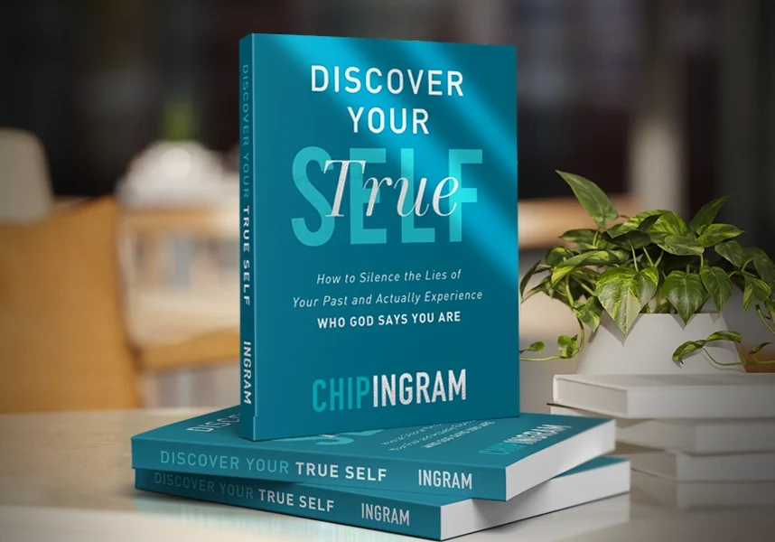 A stack of the book "Discover Your True Self" by Chip Ingram on a white table next to a potted plant.